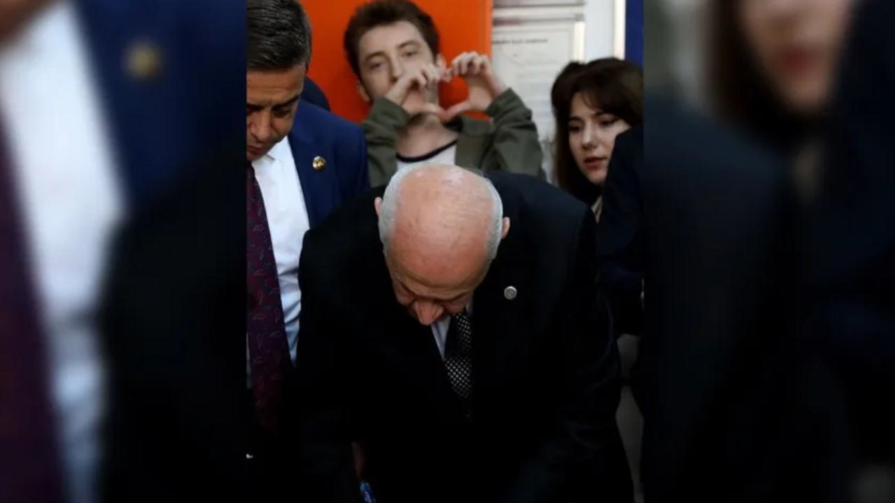 Youth makes a heart shape behind Bahçeli during voting